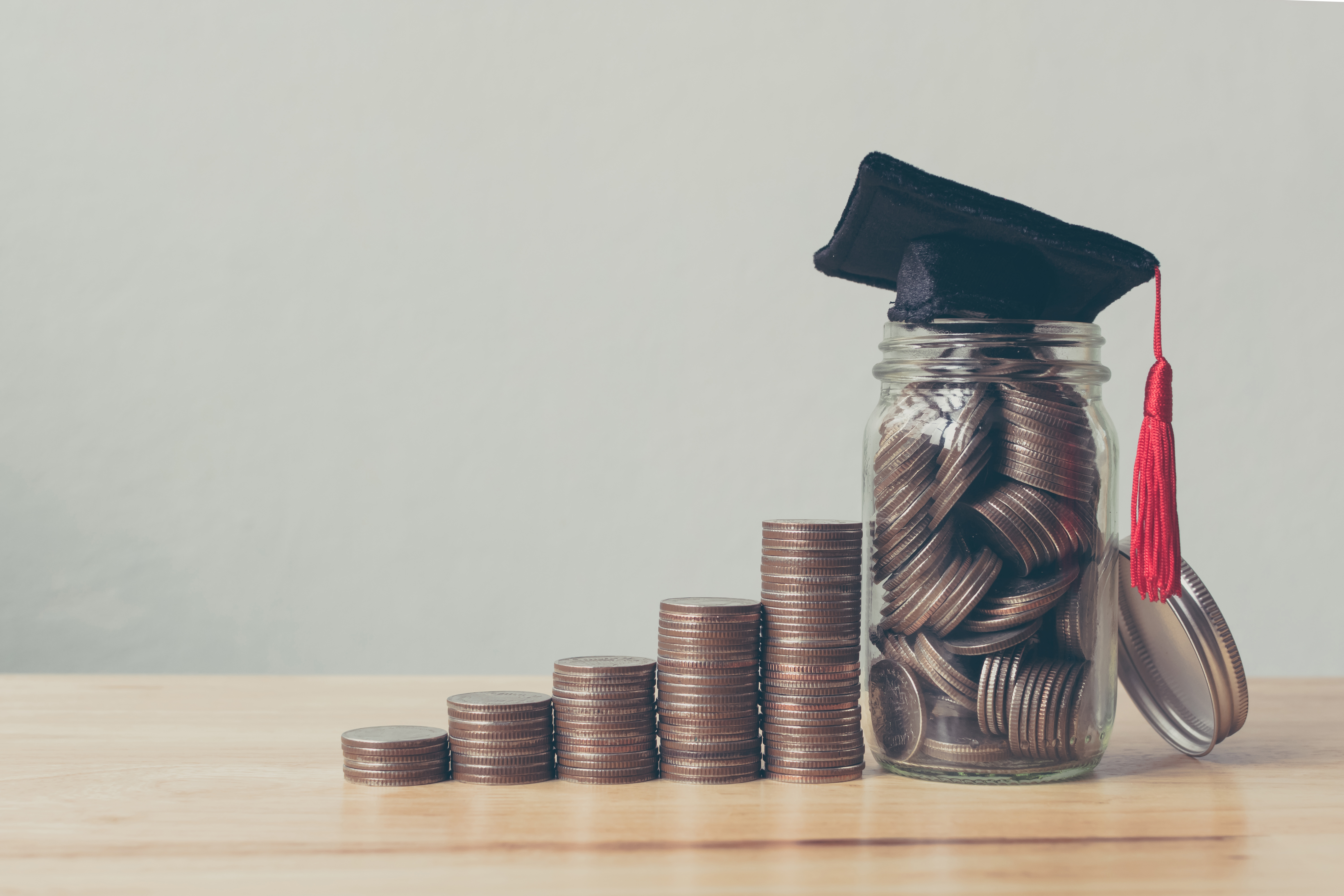 A stack of coins increasing in value with a graduation cap at the highest stack