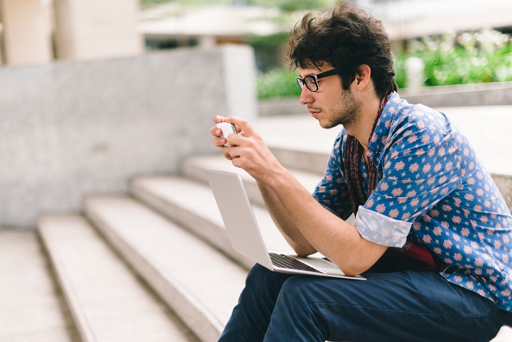 A student on their phone and laptop researching scholarships