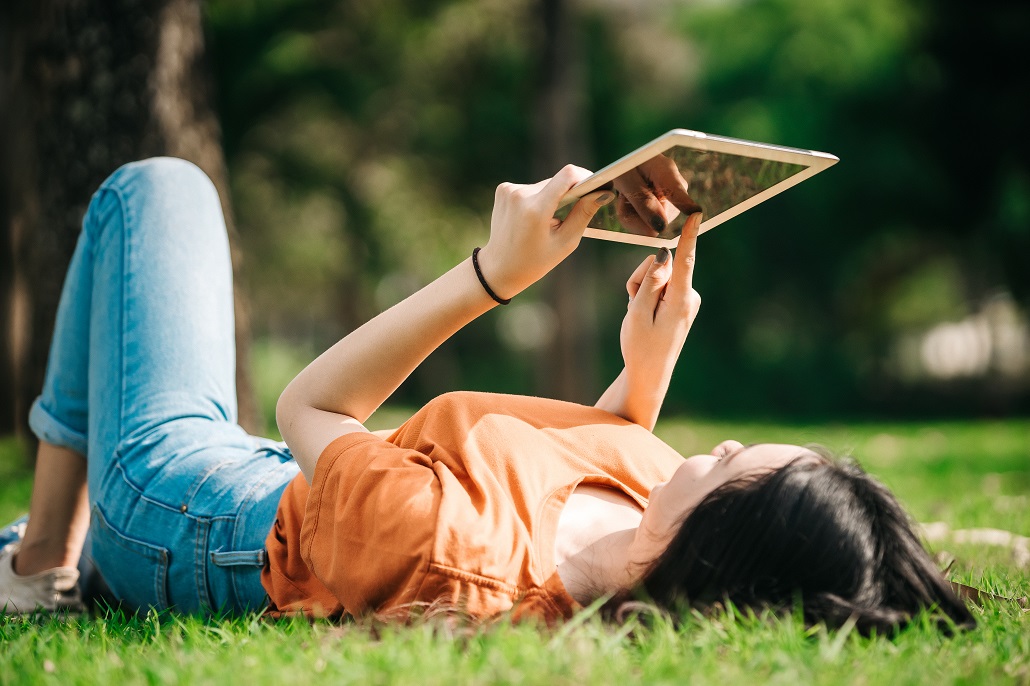 Student using tablet in the grass to look for summer job
