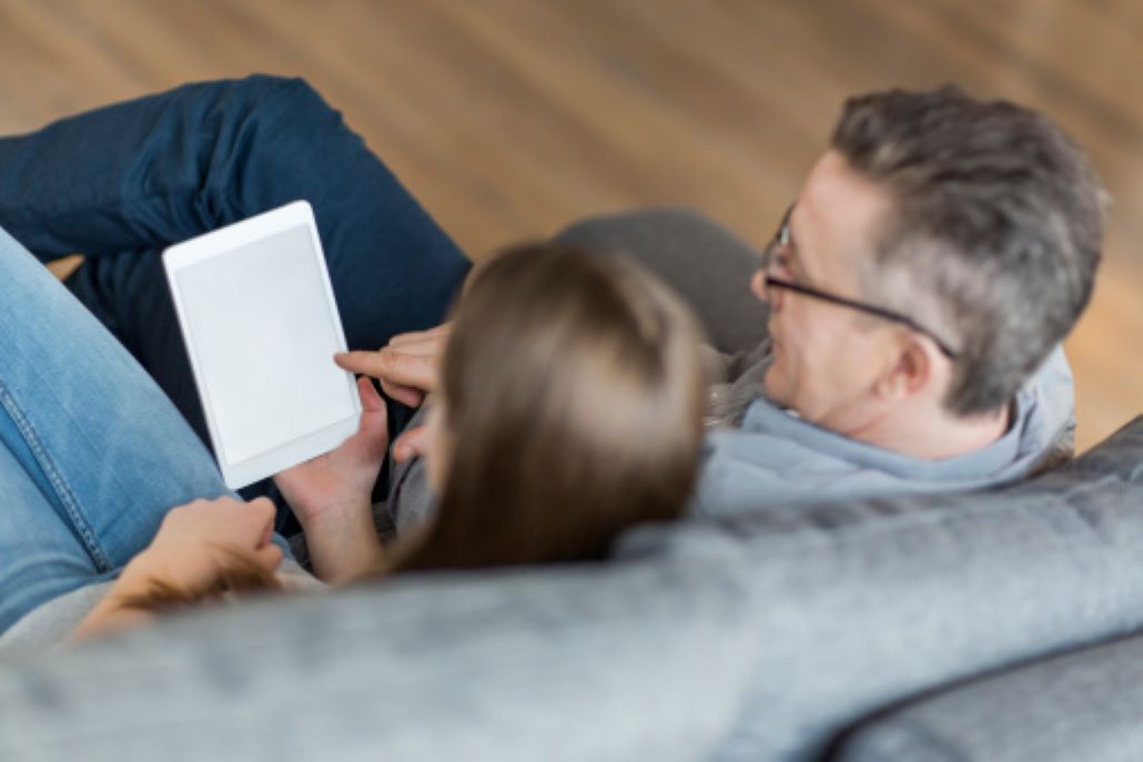 Father and daughter sitting on couch reading about financial aid on a tablet