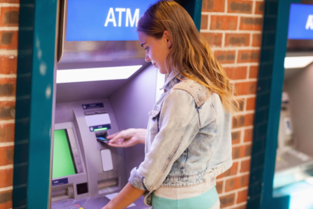 Young woman getting money at an ATM to pay for extra college costs