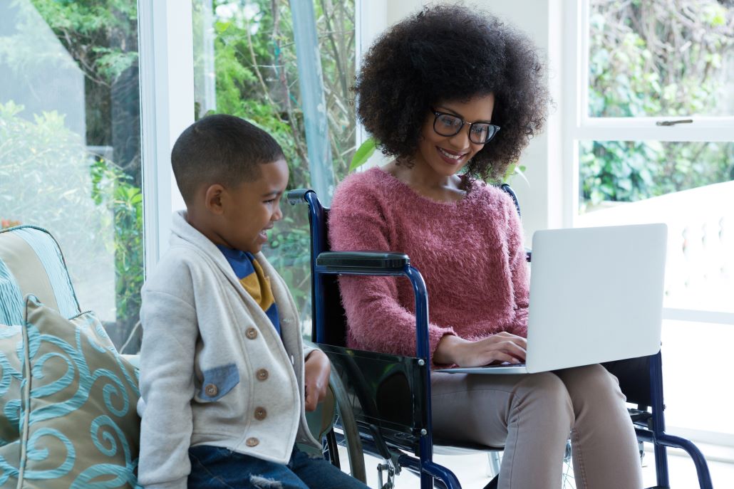 Young boy smiling next to woman working on laptop in wheelchair