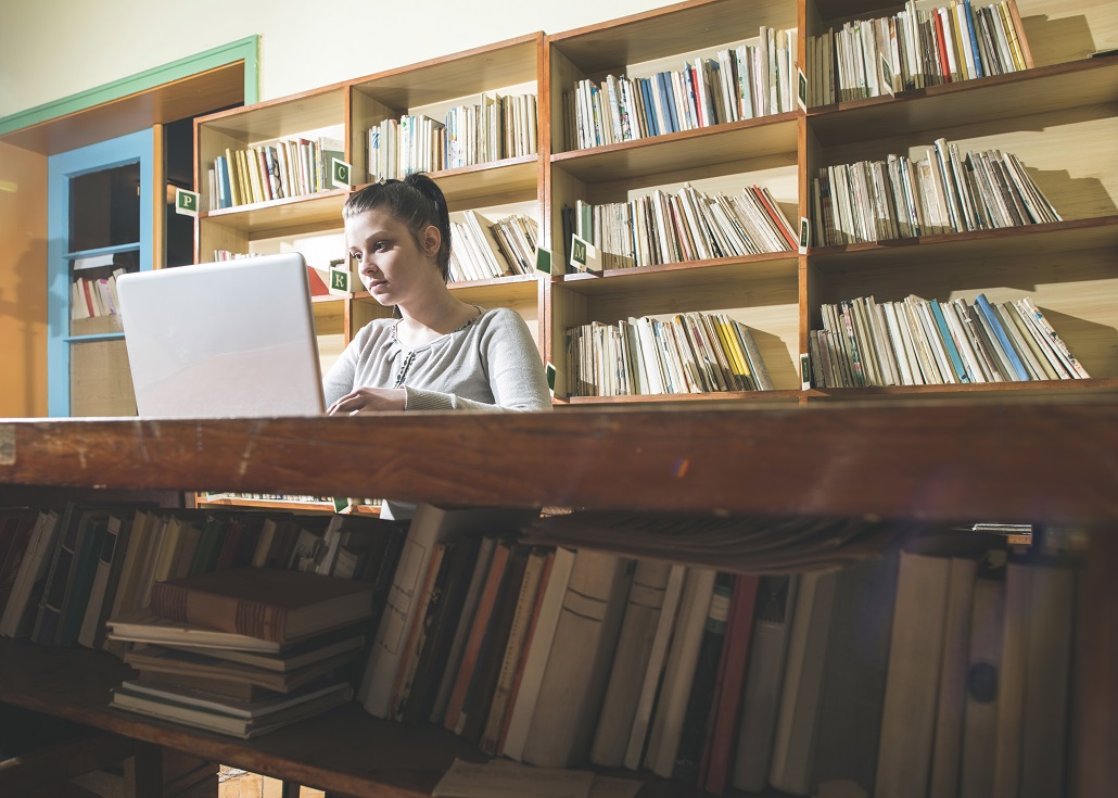 Teenage girl in library finishing her college applications on a laptop