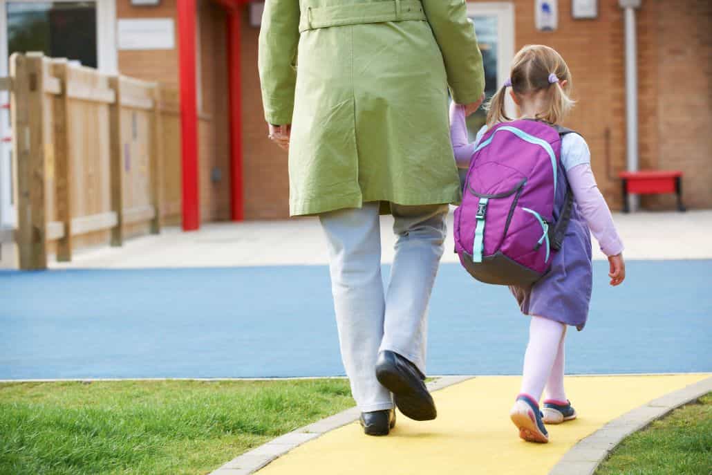 Little girl with backpack being walked to school by an adult