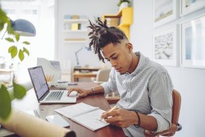 Teenager working at computer with a notebook