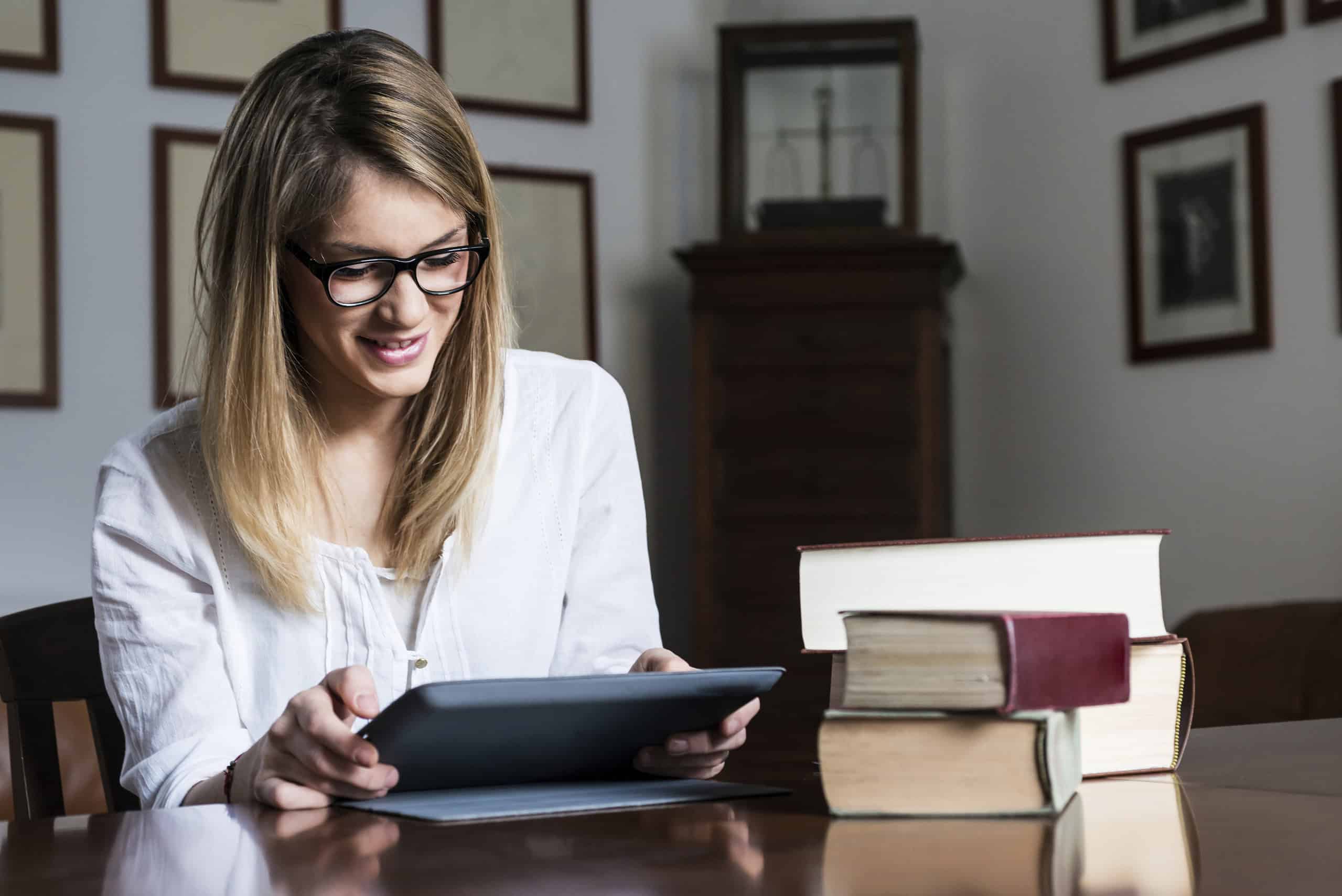 woman reading on a tablet with books next to her